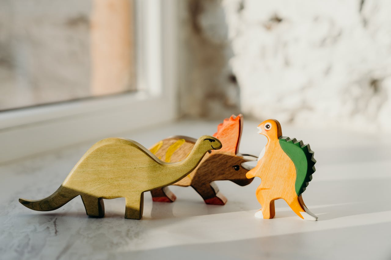 Charming wooden dinosaur toys placed on a surface, highlighted by gentle sunlight.