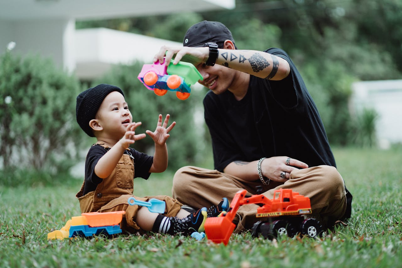 Young father and son enjoying playtime with toy cars in a sunny garden setting.