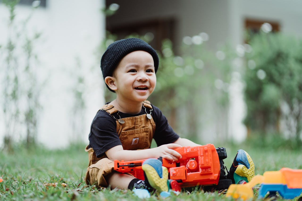 Happy child playing with colorful plastic toys in the yard, enjoying a sunny day outdoors.