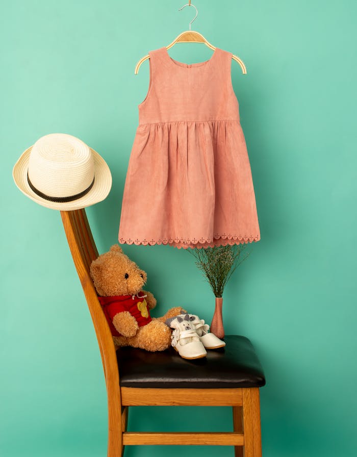 Home Stylish clothes on hanger above hat and shoes with soft bear on chair near bright wall