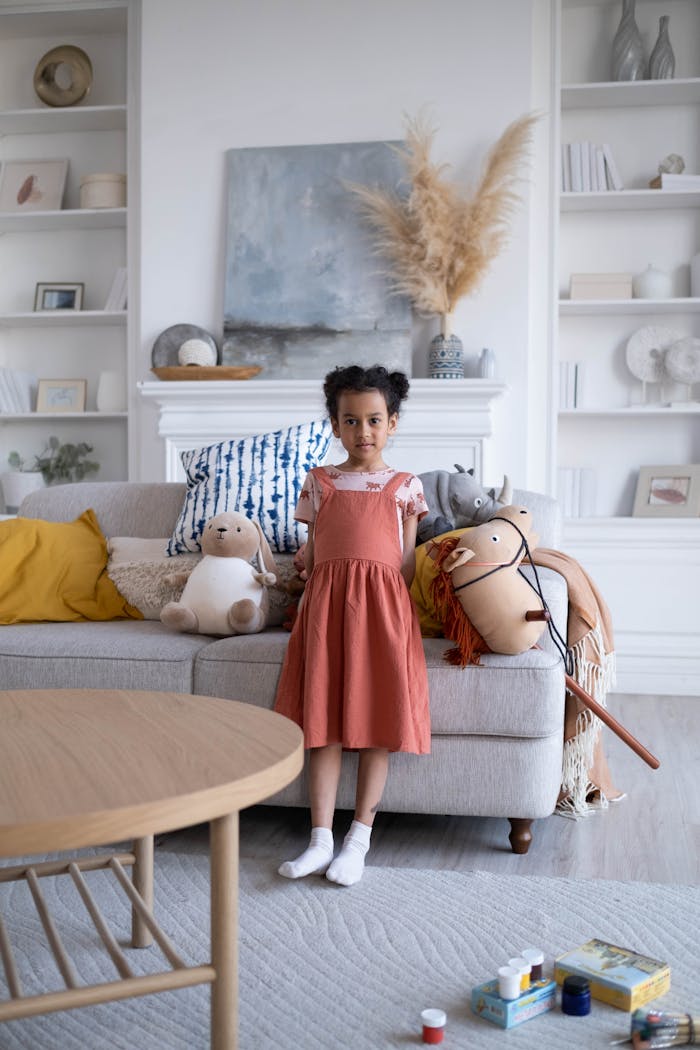 Young girl stands in a well-decorated living room with toys and decor.